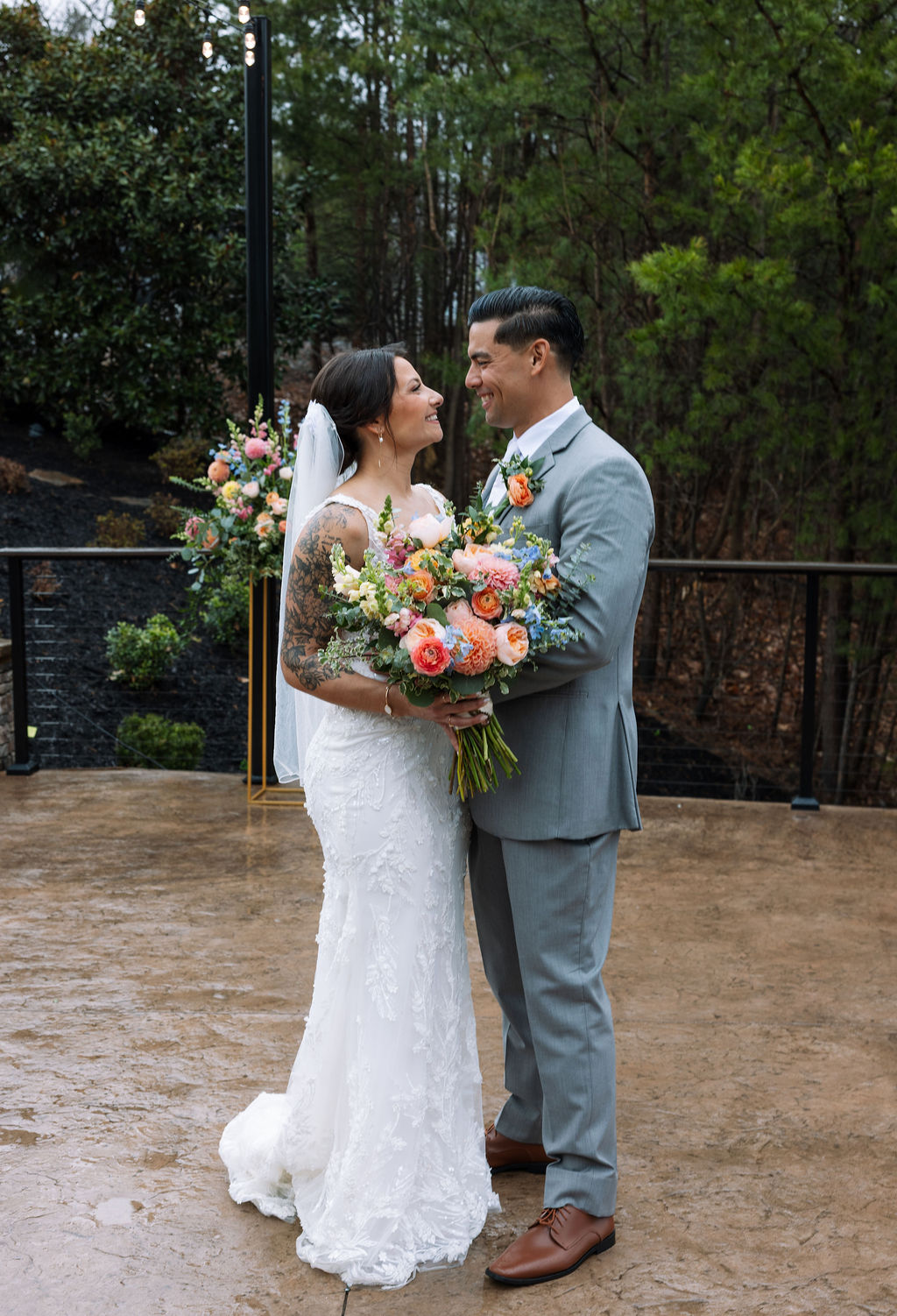 Bride and groom standing together with bouquet on a rainy day at The Magnolia Wedding Venue, surrounded by trees