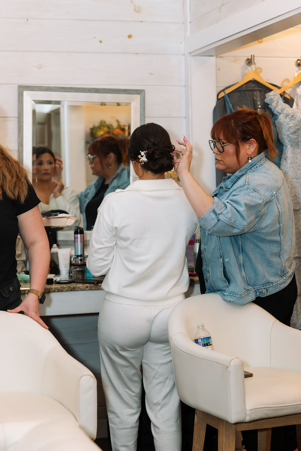 Hair stylist placing finishing touches on the bride’s updo in a softly lit bridal suite
