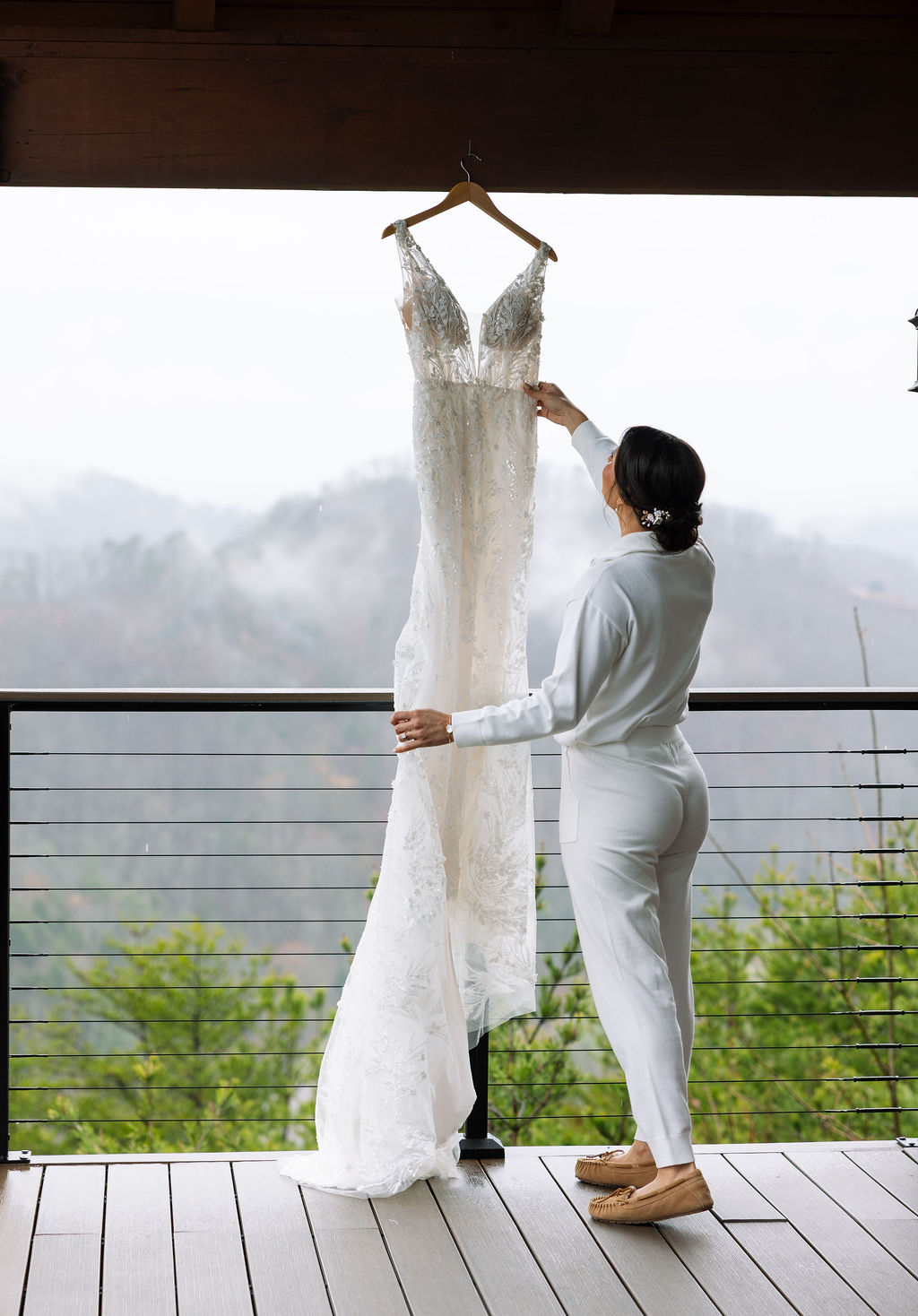 Bride adjusts lace wedding dress on a hanger at The Magnolia Wedding Venue with a mountain view in the background