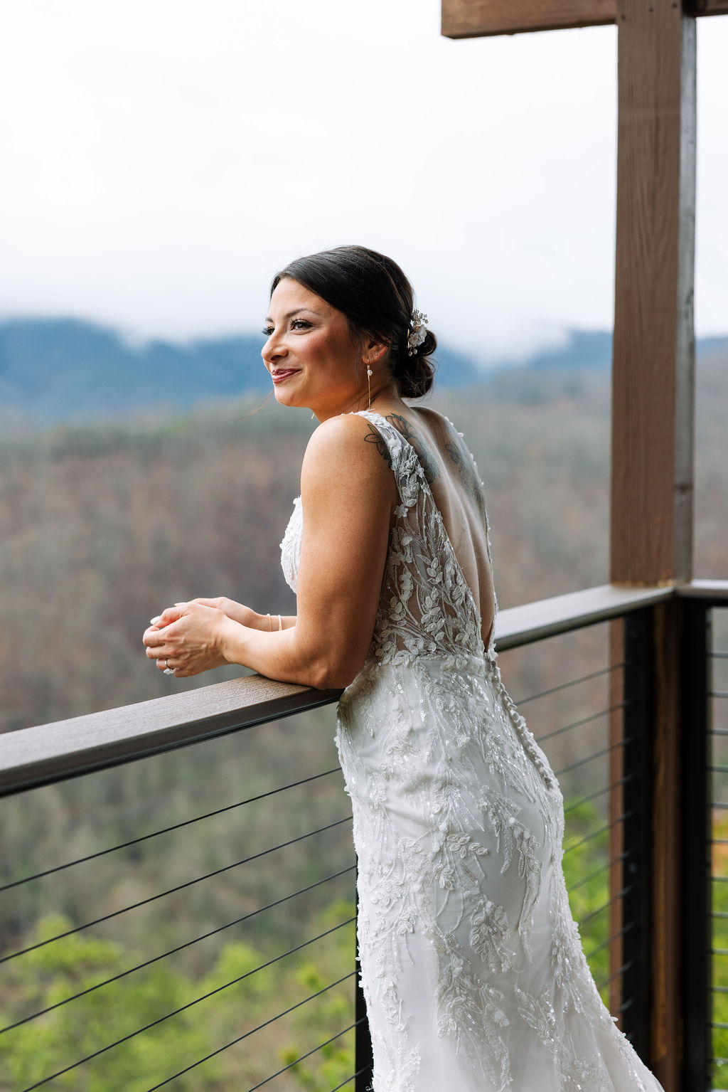 Bride leaning on balcony railing overlooking the mountains on a cloudy wedding day
