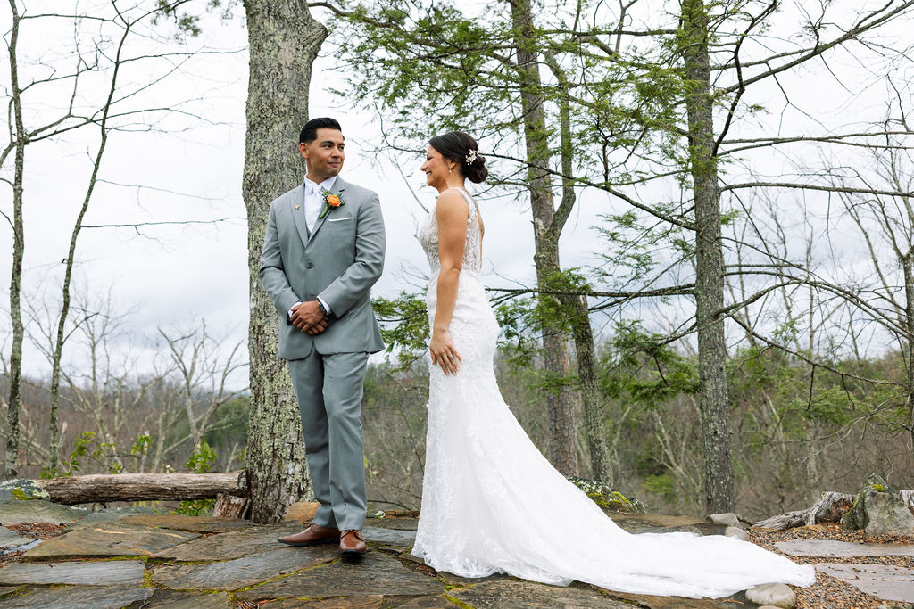 Bride and groom smiling at each other on a mountain overlook during their first look
