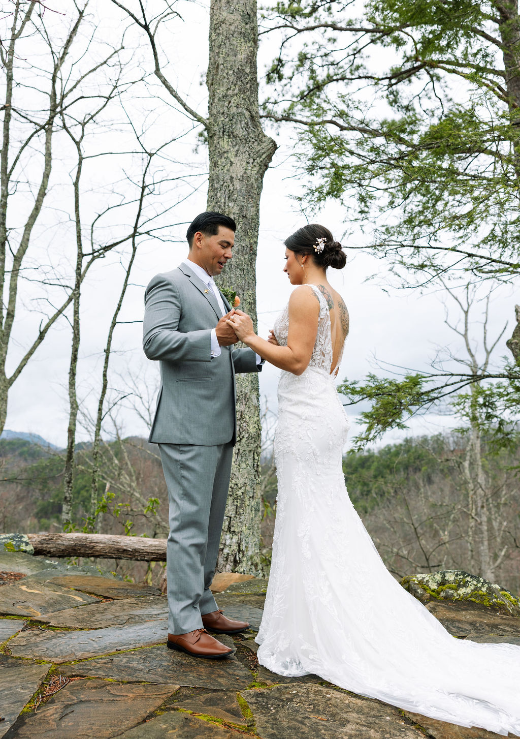Bride and groom hold hands and smile at each other on a mountain overlook at The Magnolia Wedding Venue

