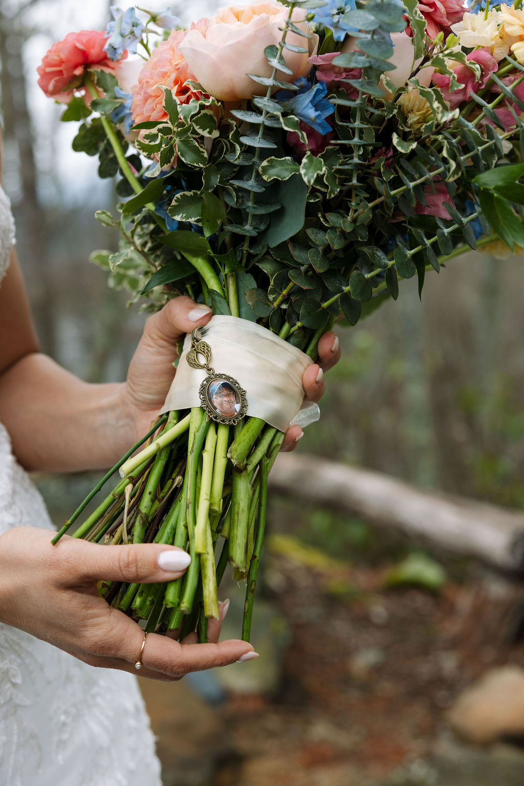 Close-up of bridal bouquet with garden roses, eucalyptus, and a photo charm wrapped around the stems
