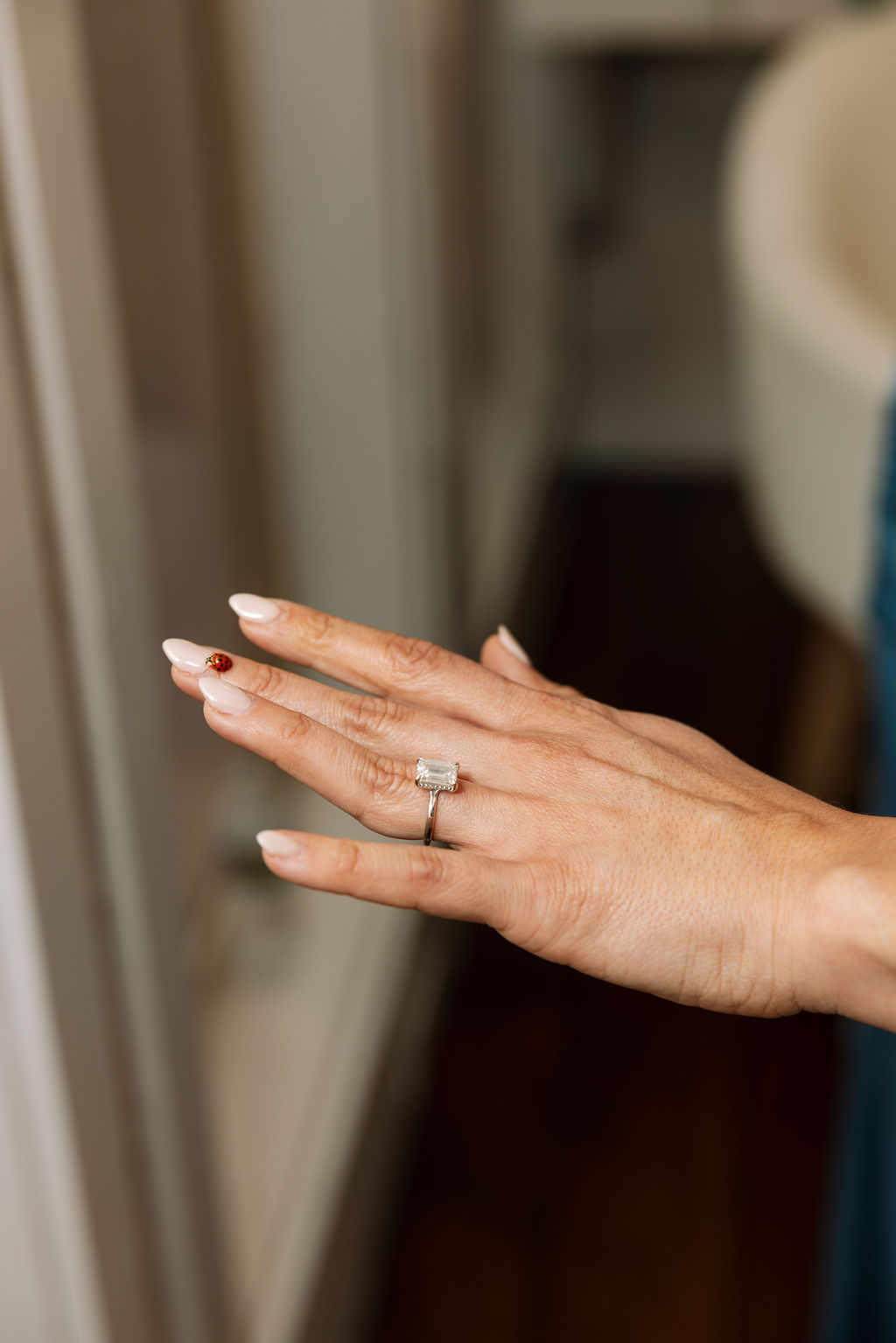 Bride’s hand with emerald-cut engagement ring and soft neutral manicure, a small ladybug resting on her finger
