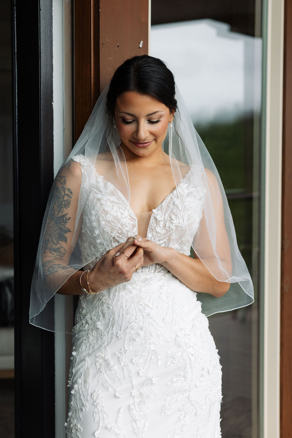 Bride standing by a window adjusting her ring, wearing a lace wedding dress and veil at The Magnolia Wedding Venue
