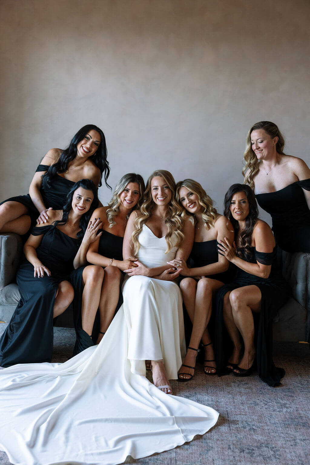 Bride sitting with bridesmaids in black dresses during wedding morning portraits