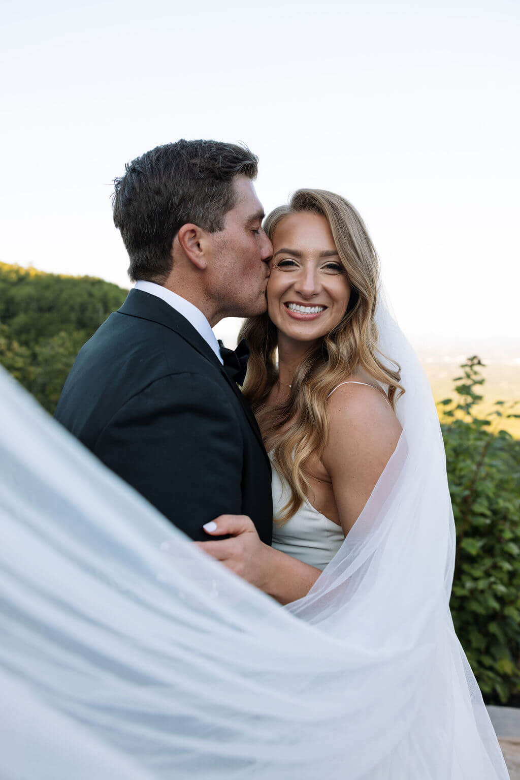 Bride smiling during wedding portraits with veil wrapped around the couple at a Knoxville wedding venue