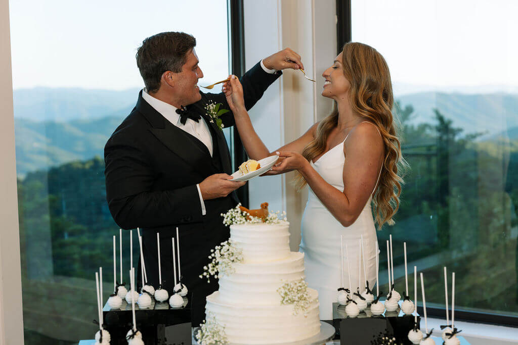 Bride and groom feeding each other cake with mountain views behind them
