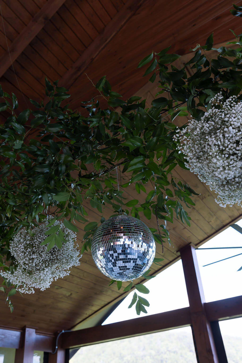 Wedding reception ceiling decor with disco balls and greenery installation