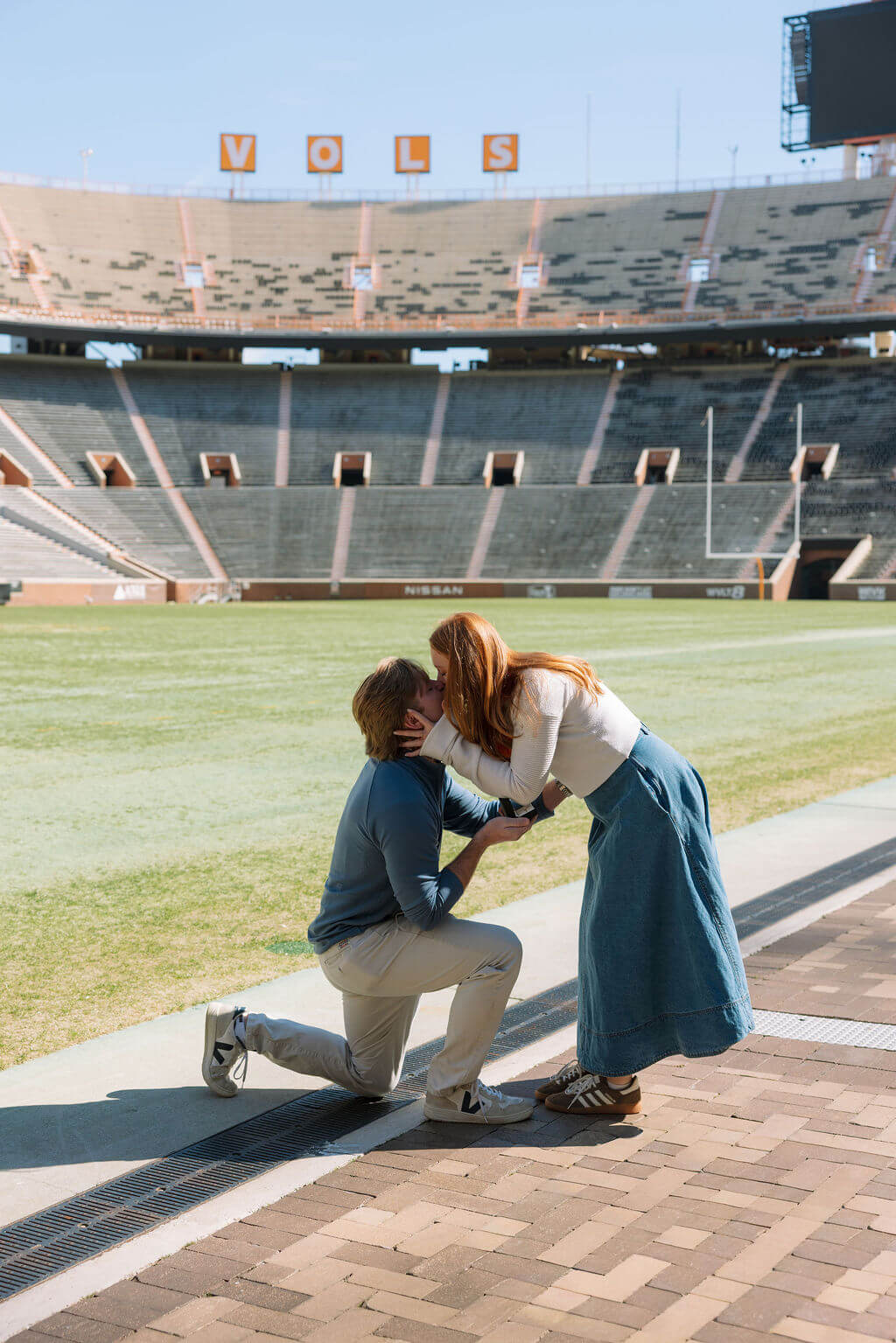 Couple kissing after a proposal at Neyland Stadium in Knoxville, Tennessee on the football field.