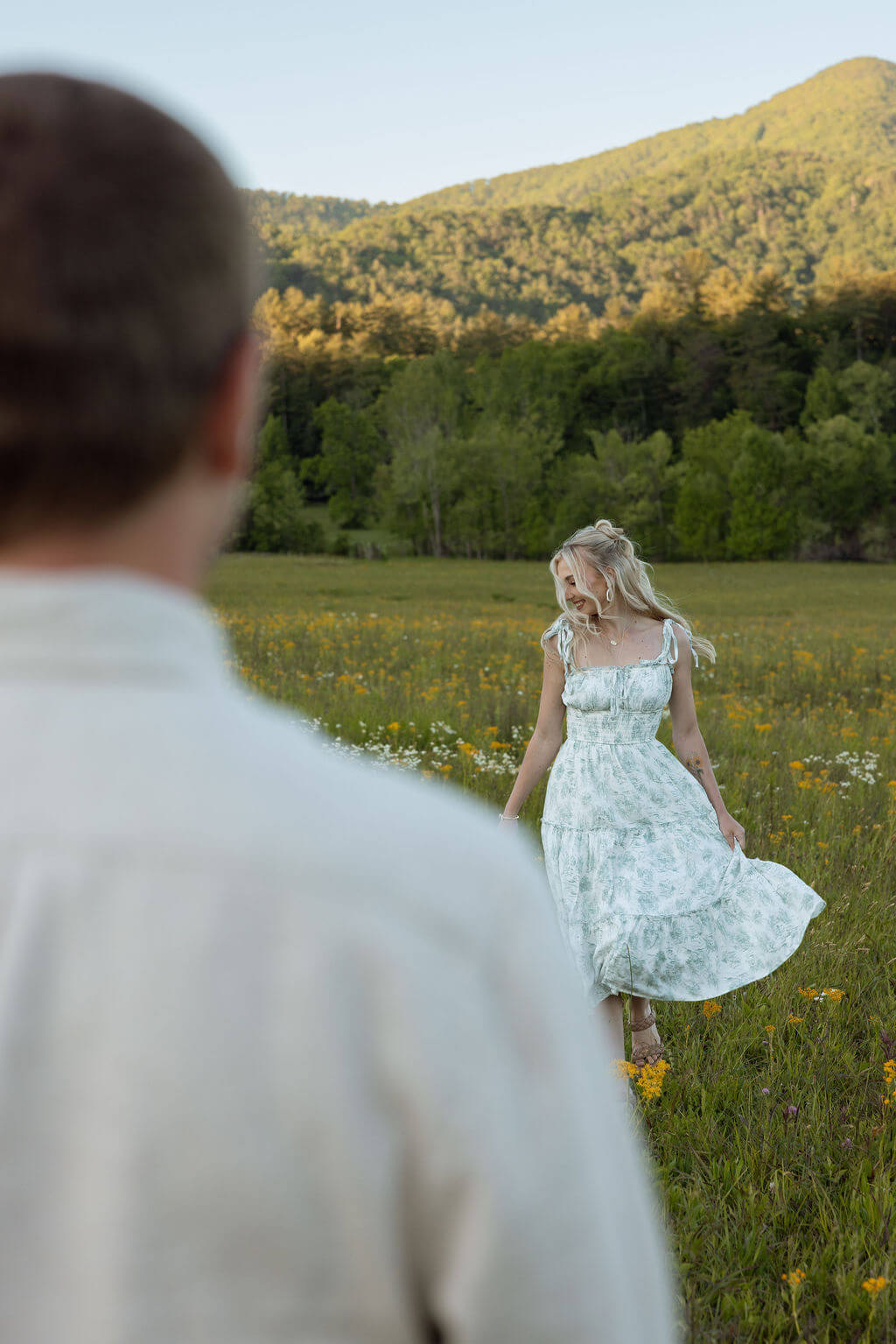 Bride-to-be spinning in a wildflower field during a Knoxville, Tennessee couples session with mountain views in the background.