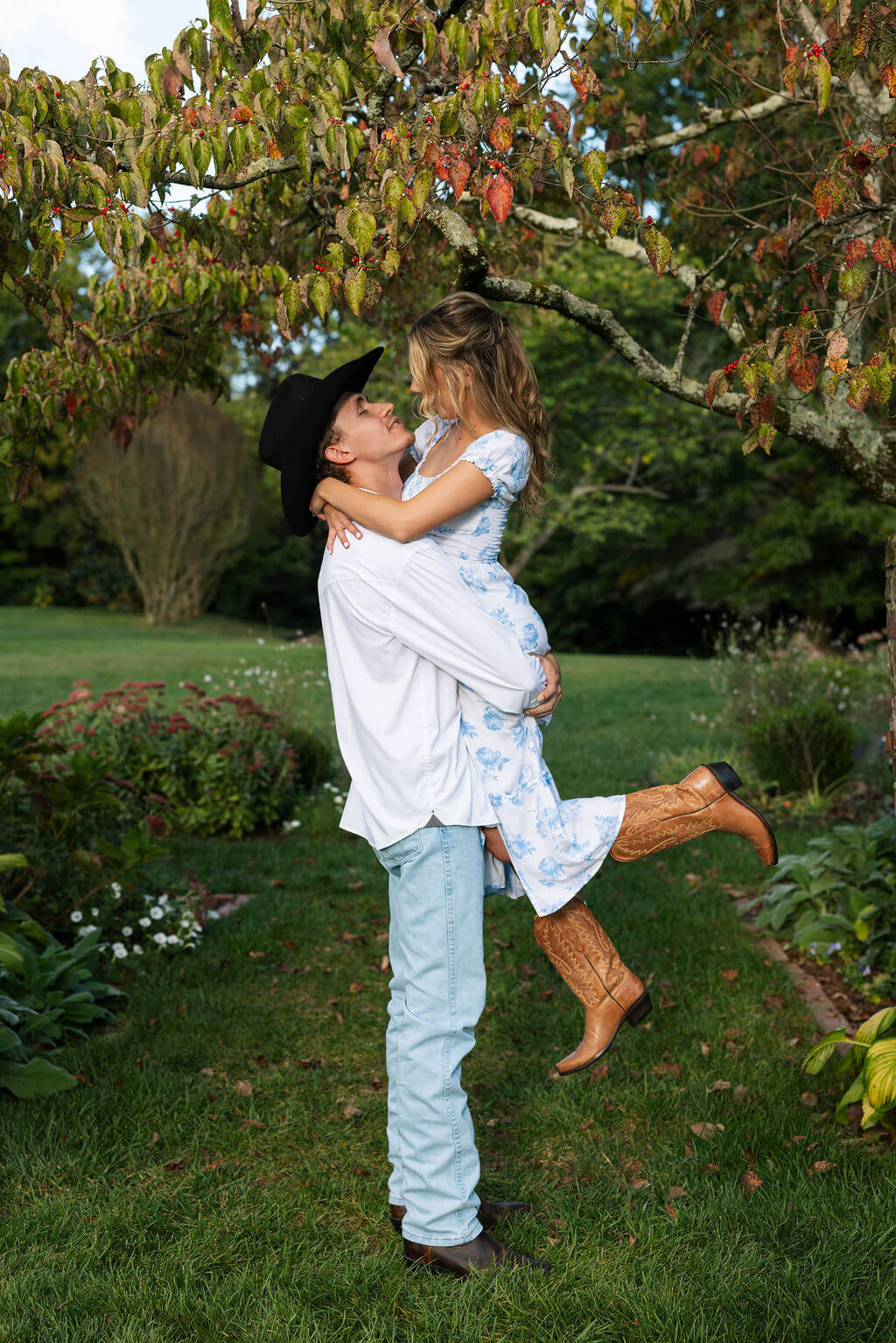 Playful engagement photos at Maple Grove Estate with groom lifting bride beneath flowering trees