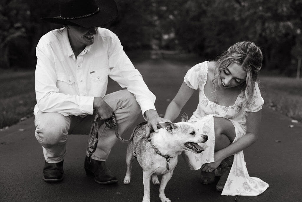 Black and white engagement photos with couple petting their dog on a quiet road at Maple Grove Estate