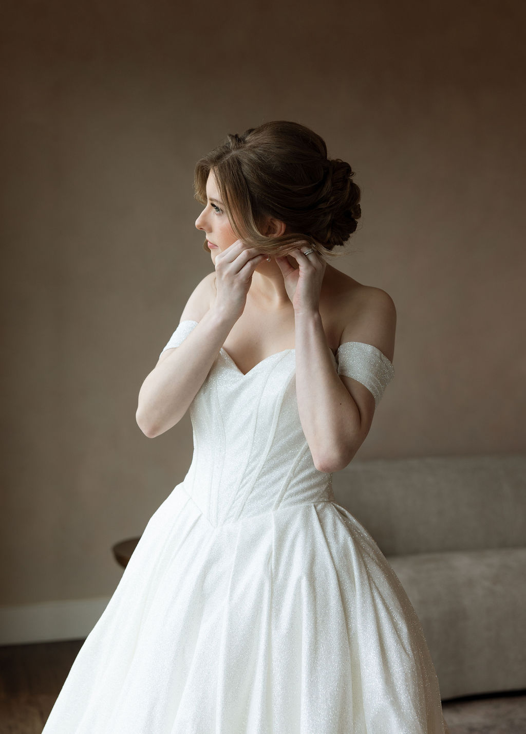 Bride putting on earrings in a softly lit bridal suite before her wedding ceremony