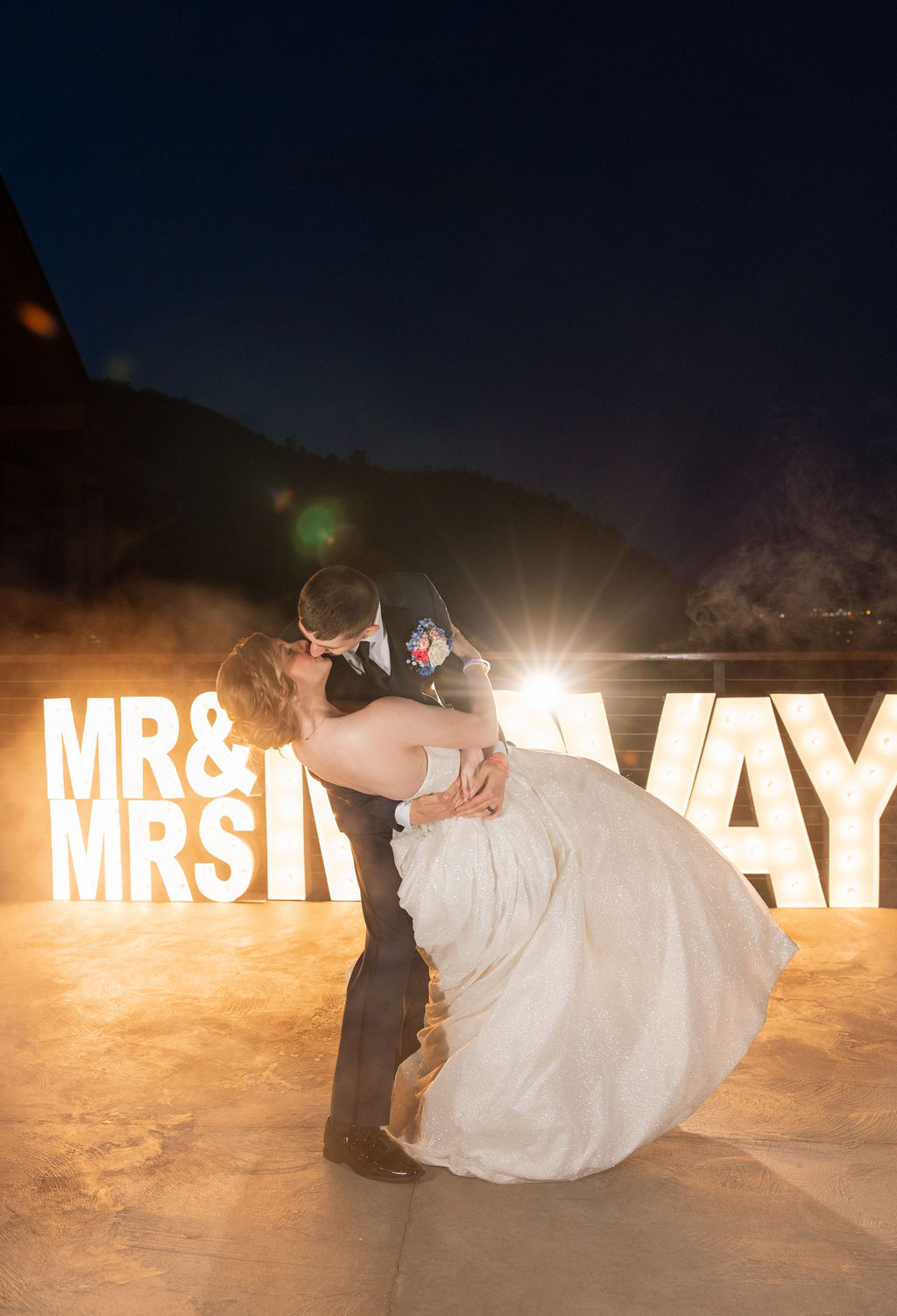 Bride and groom dipping for a kiss in front of glowing marquee letters at their Sevierville wedding venue reception