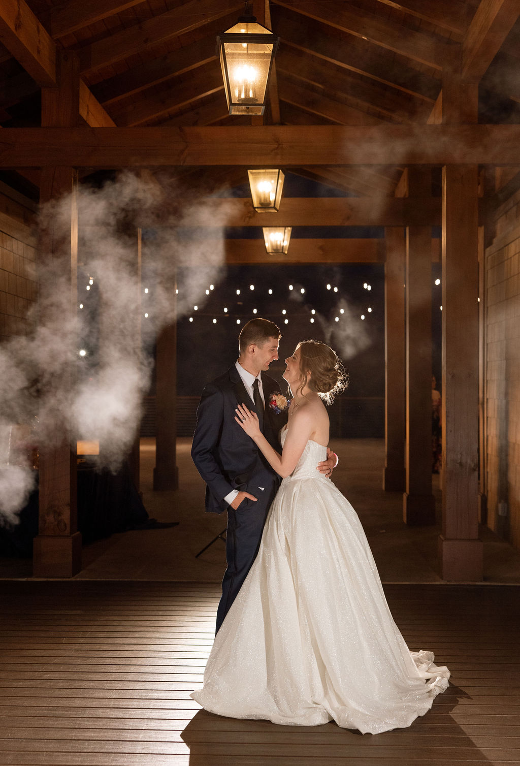 Romantic nighttime wedding portrait of bride and groom under warm lights and smoke effects during their reception