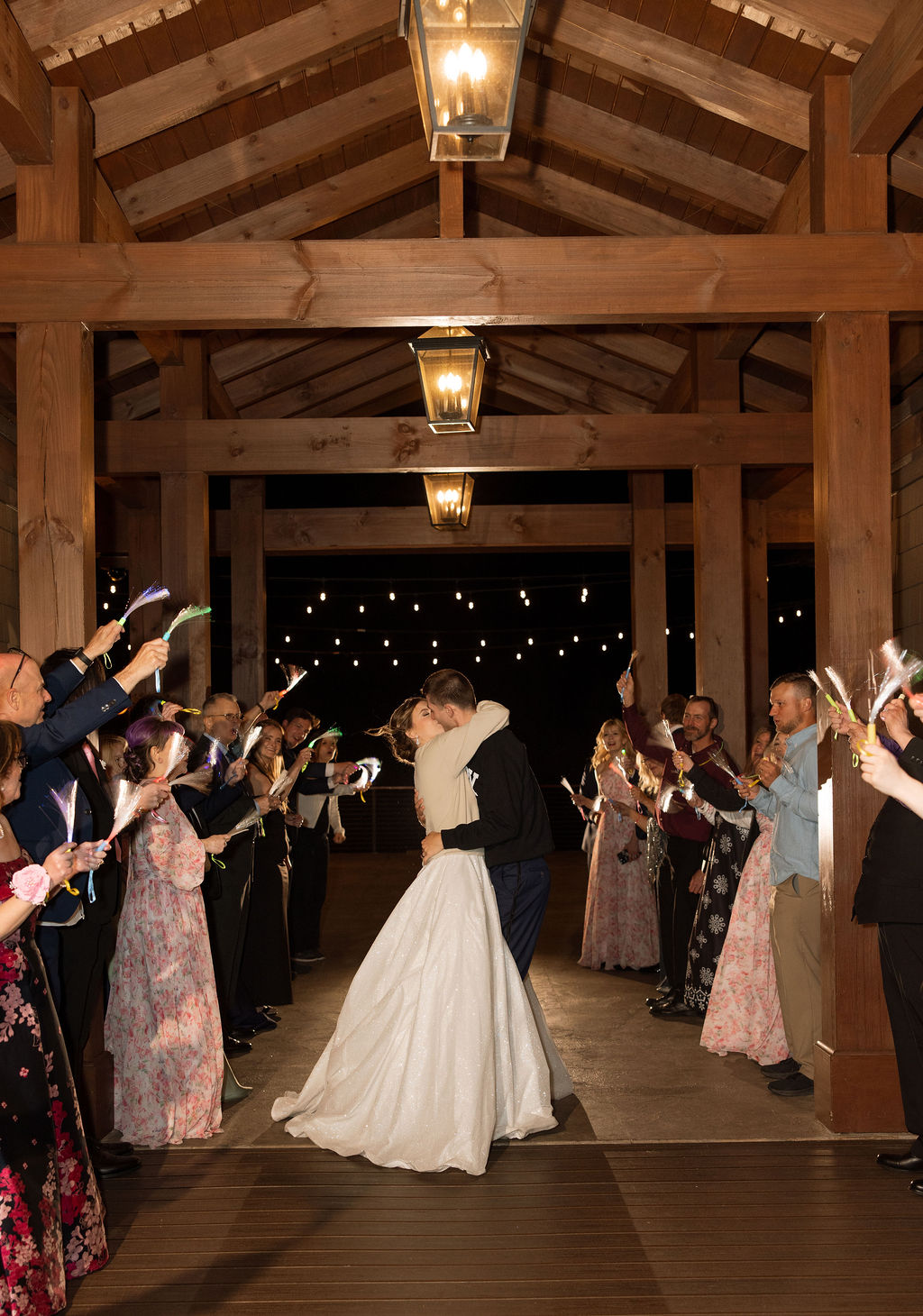 Newlyweds kissing during a sparkler exit beneath wooden beams and string lights at their Tennessee wedding reception