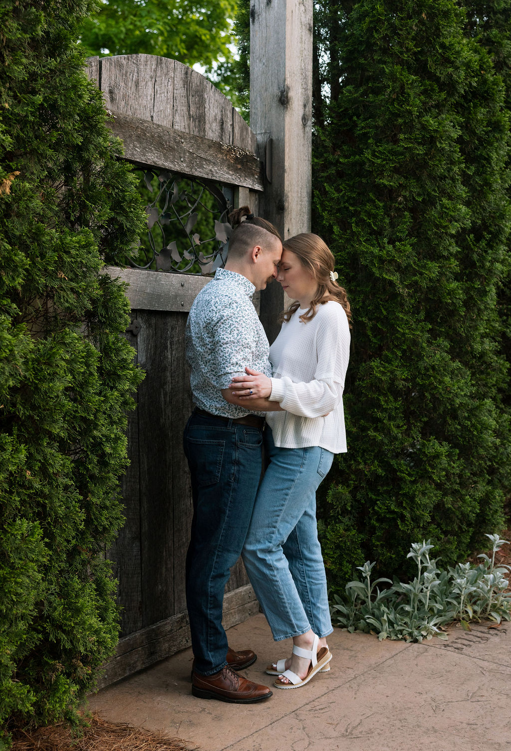 Couple stealing a quiet kiss in a doorway draped in climbing vines at Knoxville Botanical Garden, framed by weathered wood and greenery in warm evening light.