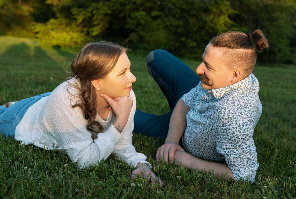 Close-up of a couple lying in the grass together at Knoxville Botanical Garden, the man gently holding the woman's face as they look at each other in warm late-day light.