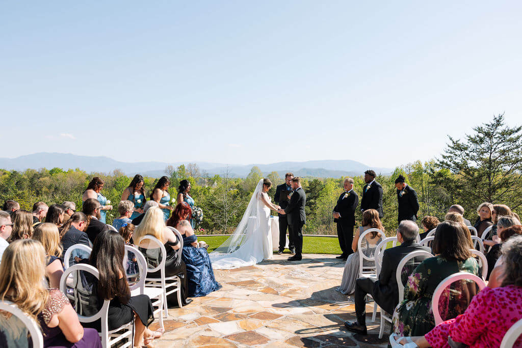 Bride and groom exchange vows at an outdoor wedding ceremony overlooking rolling green hills.