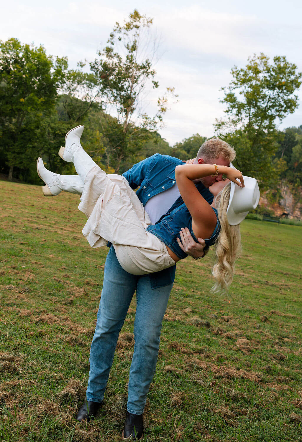 Groom lifting his partner horizontally in his arms during a playful engagement session in an open field.
