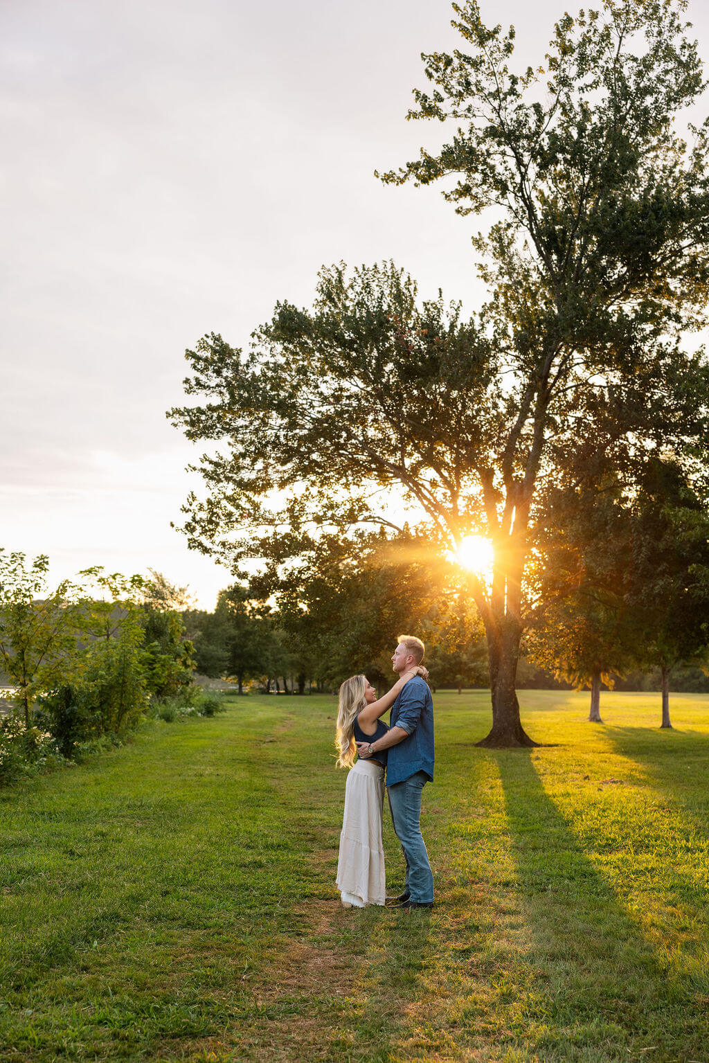 Couple standing together in an open field at sunset with long shadows stretching across the grass.