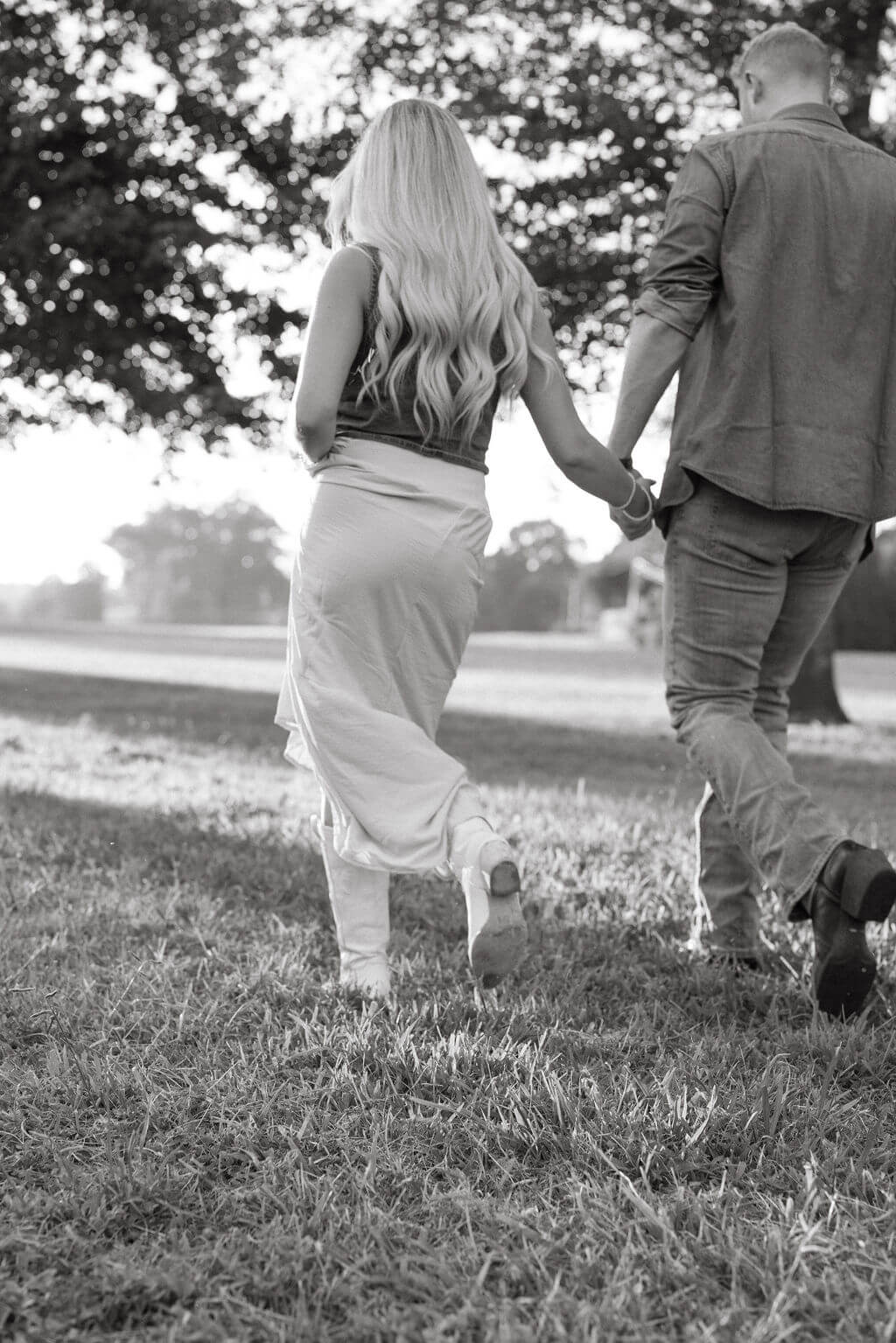 Black and white photo of a couple walking away together across a field while holding hands. The image focuses on movement and connection.