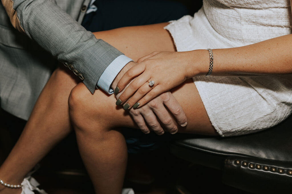 Close-up of a woman’s engagement ring as her hand rests over her fiancé’s hand during their engagement photoshoot.