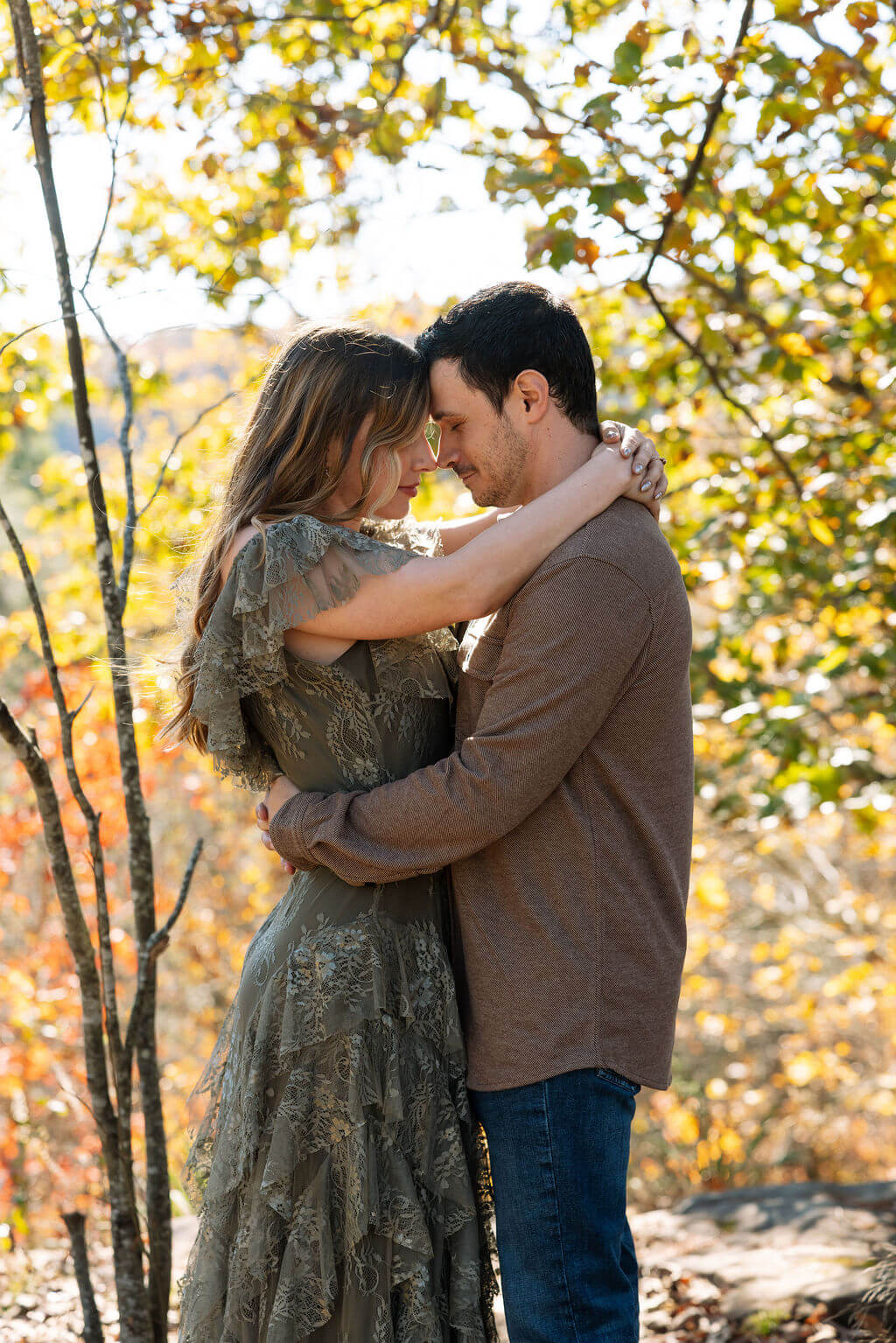 Couple holding each other under golden autumn trees during fall engagement photos in Tennessee.