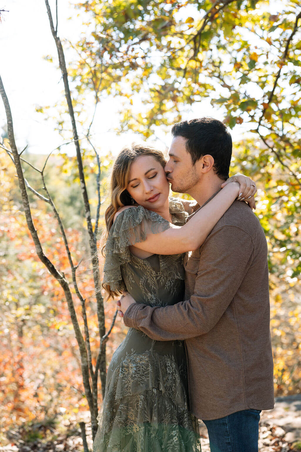 Couple cuddling under golden leaves during fall engagement photos at a rocky Tennessee waterfall location.