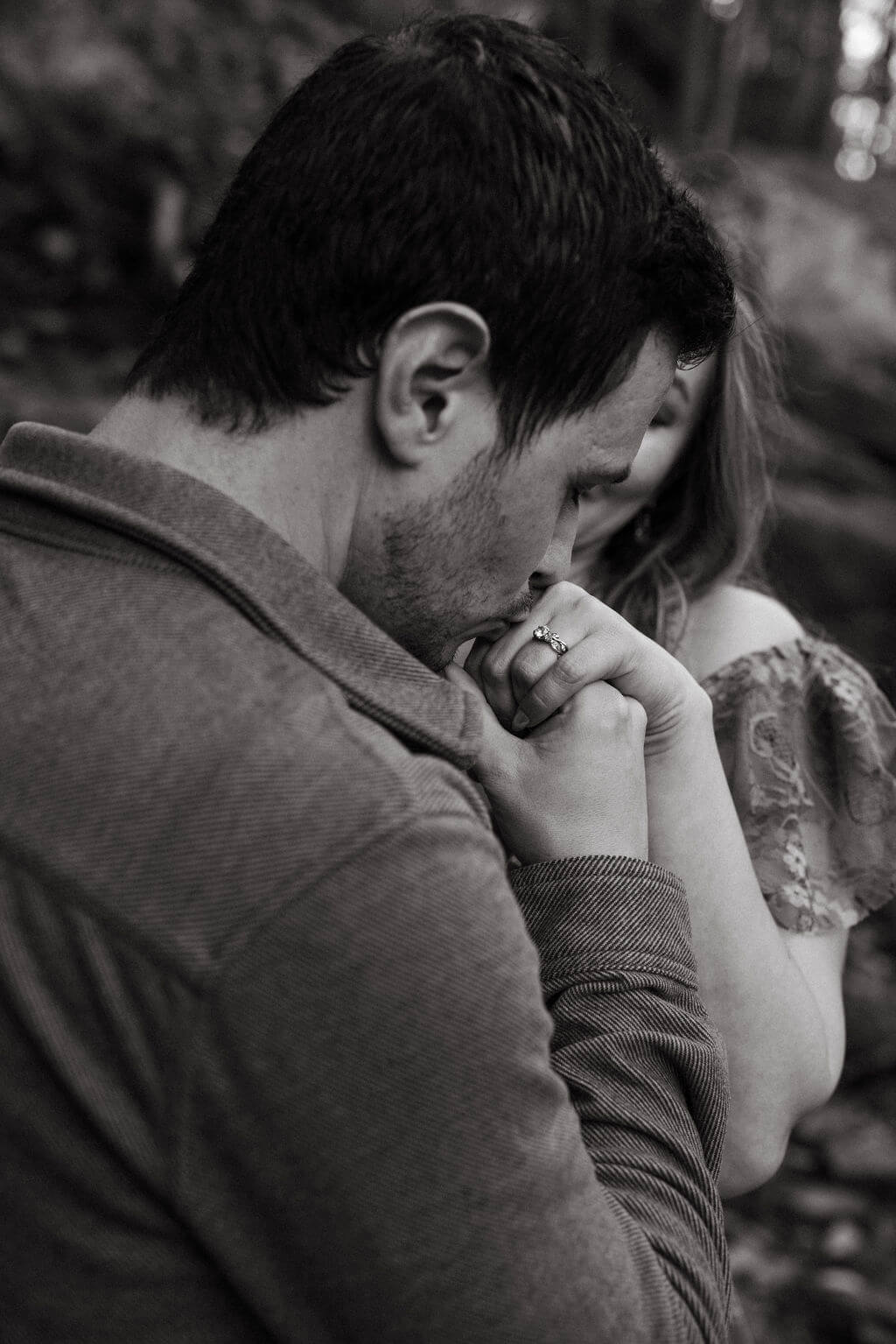 Black and white photo of a man kissing his partner’s hand during intimate fall engagement photos.