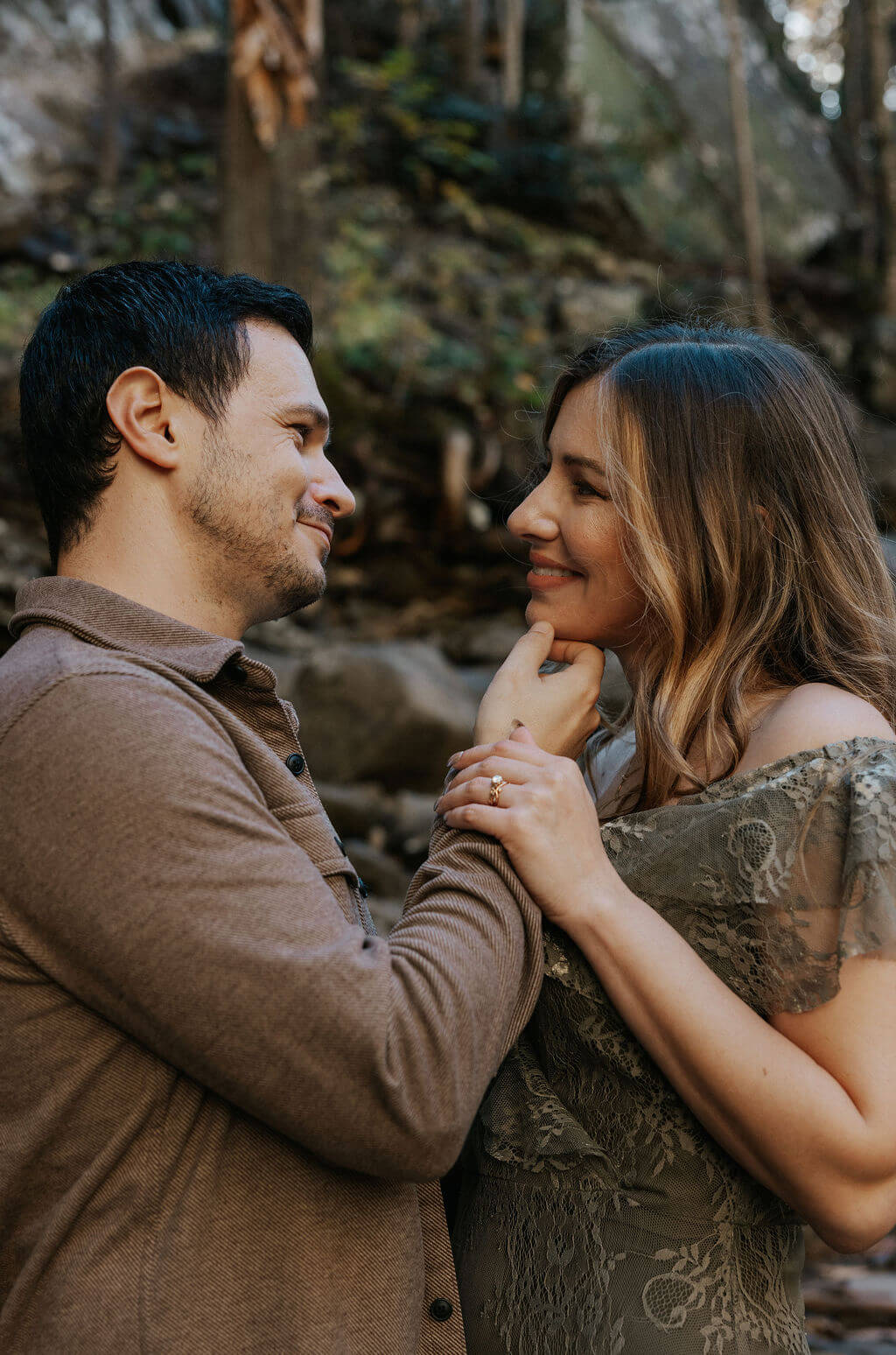 Couple smiling at each other while cuddling during cozy fall engagement photos.