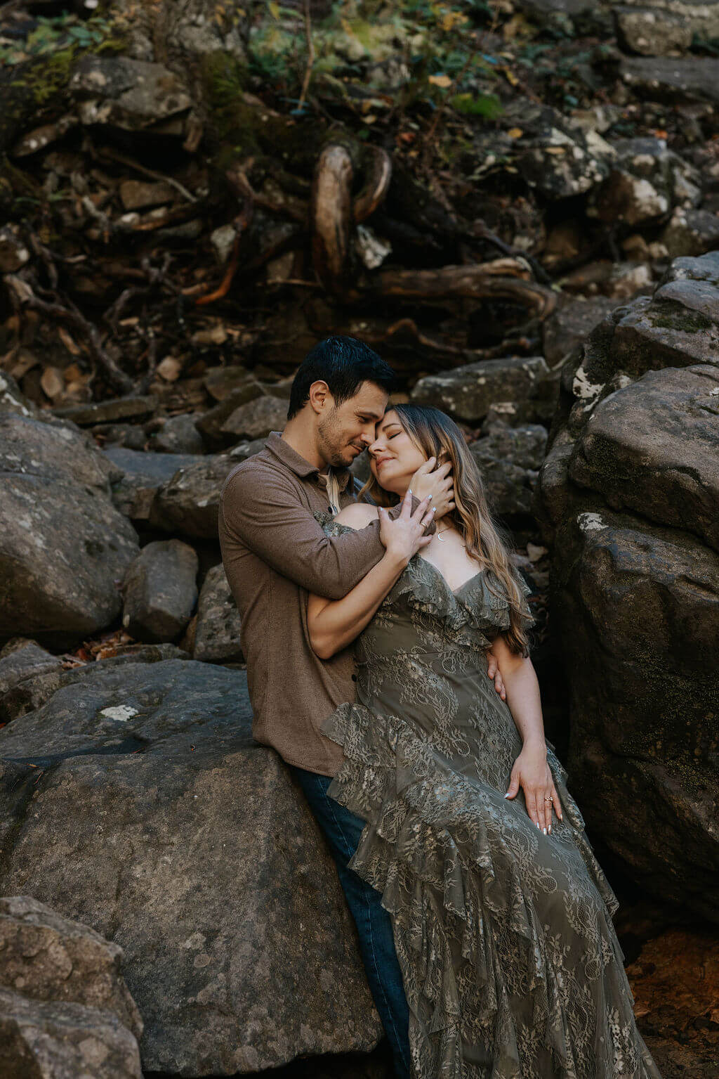 Couple cuddling on large rocks during romantic fall engagement photos in the woods.