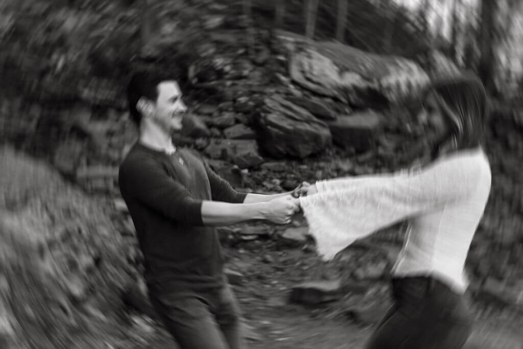 Black and white motion blur photo of a couple spinning together during playful fall engagement photos.