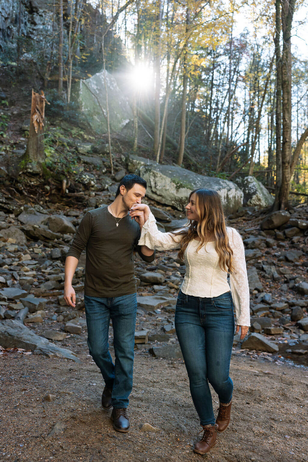 Couple walking hand in hand through a rocky wooded trail during fall engagement photos in Tennessee.