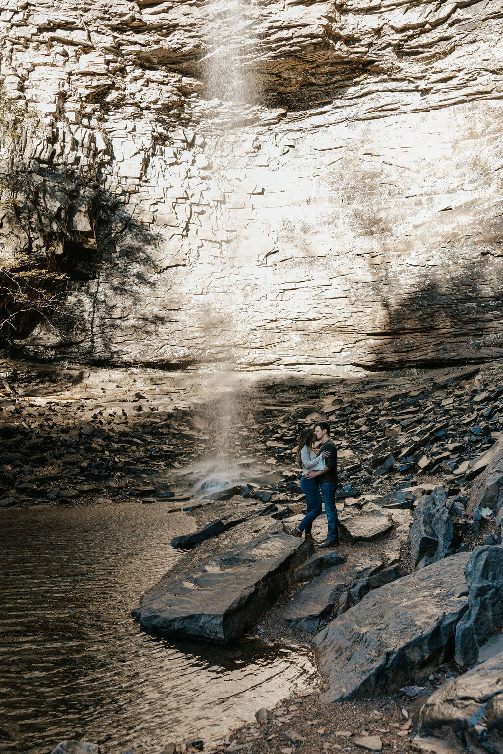 Couple standing together beneath a waterfall during adventurous fall engagement photos in Tennessee.