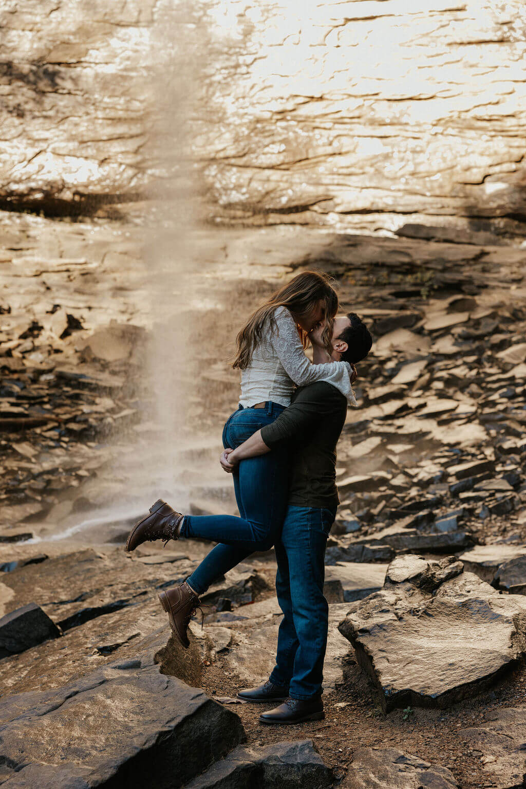 Couple kissing in front of a waterfall during adventurous fall engagement photos in Tennessee.