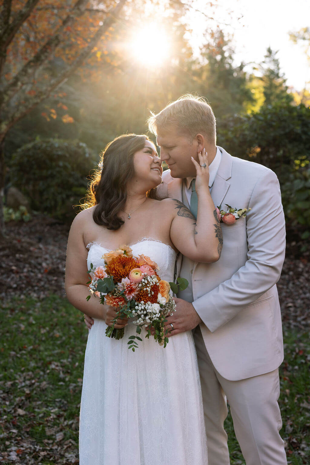 Newlyweds share a close embrace while holding an orange and white fall wedding bouquet.