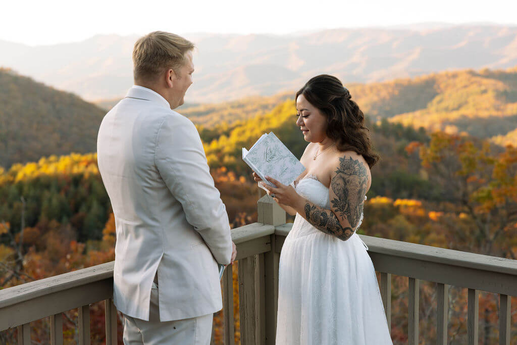Bride reads handwritten vows to her partner on a deck overlooking the colorful Tennessee mountains.