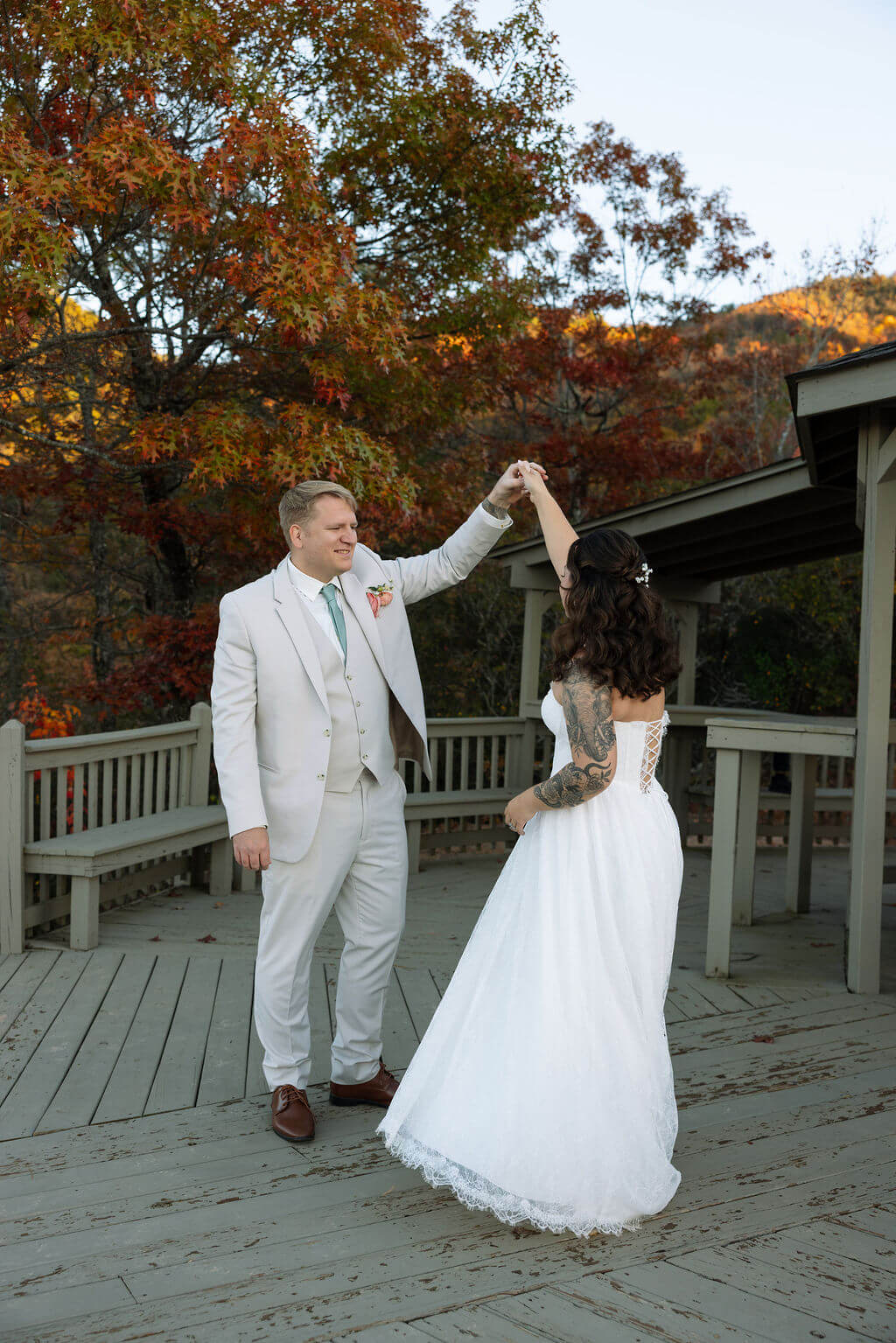 Newlyweds dance beneath a wooden gazebo surrounded by brilliant red and orange autumn trees.