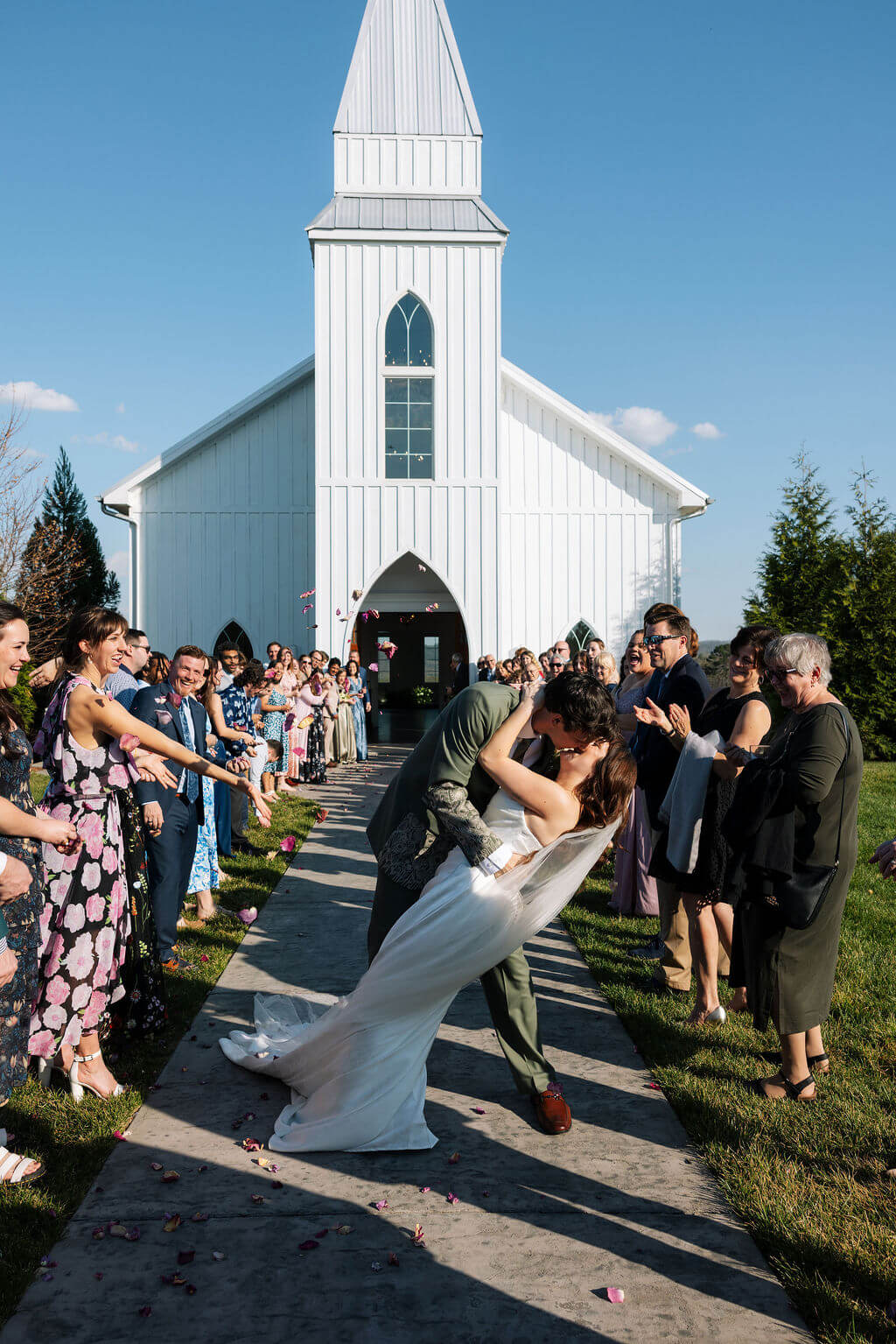 Newlyweds running through a celebratory wedding exit outside a white chapel.