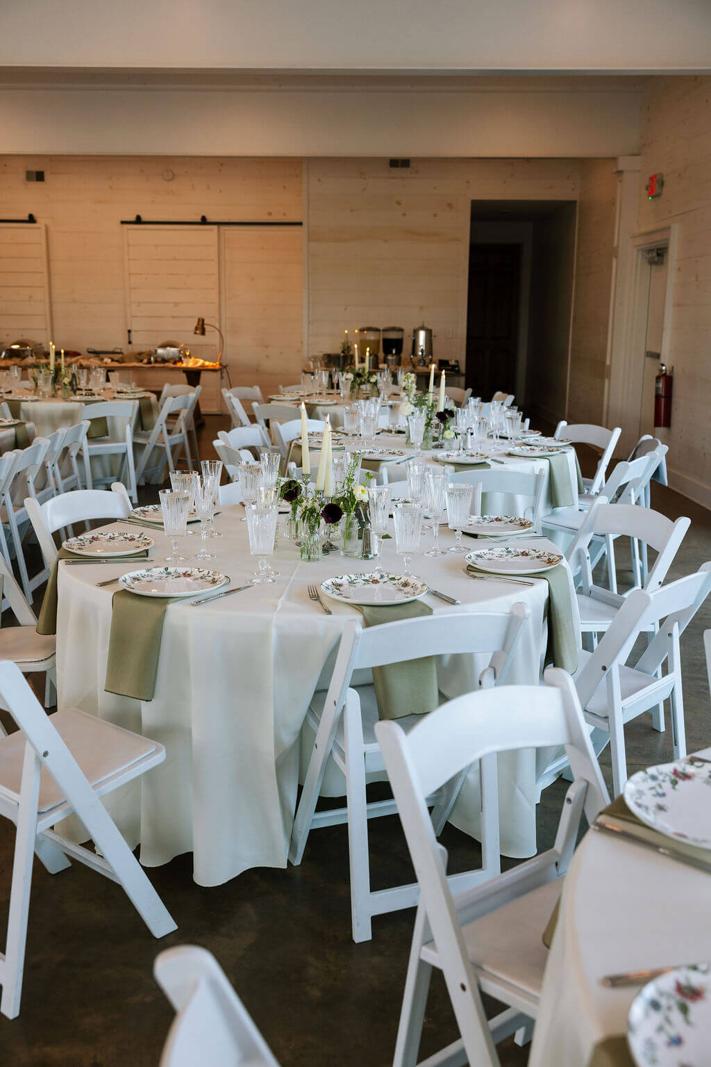 Wedding reception tables arranged with white chairs and neutral décor inside a modern event space.