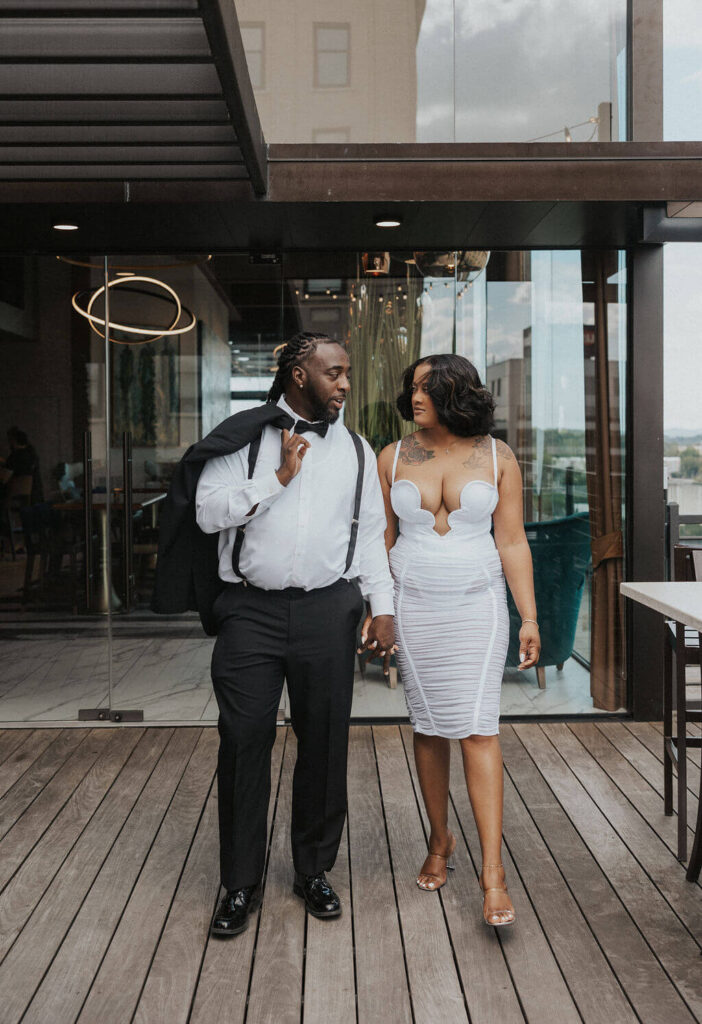 Couple walking hand in hand across a modern rooftop patio during stylish engagement photos at one of the downtown Knoxville bars.