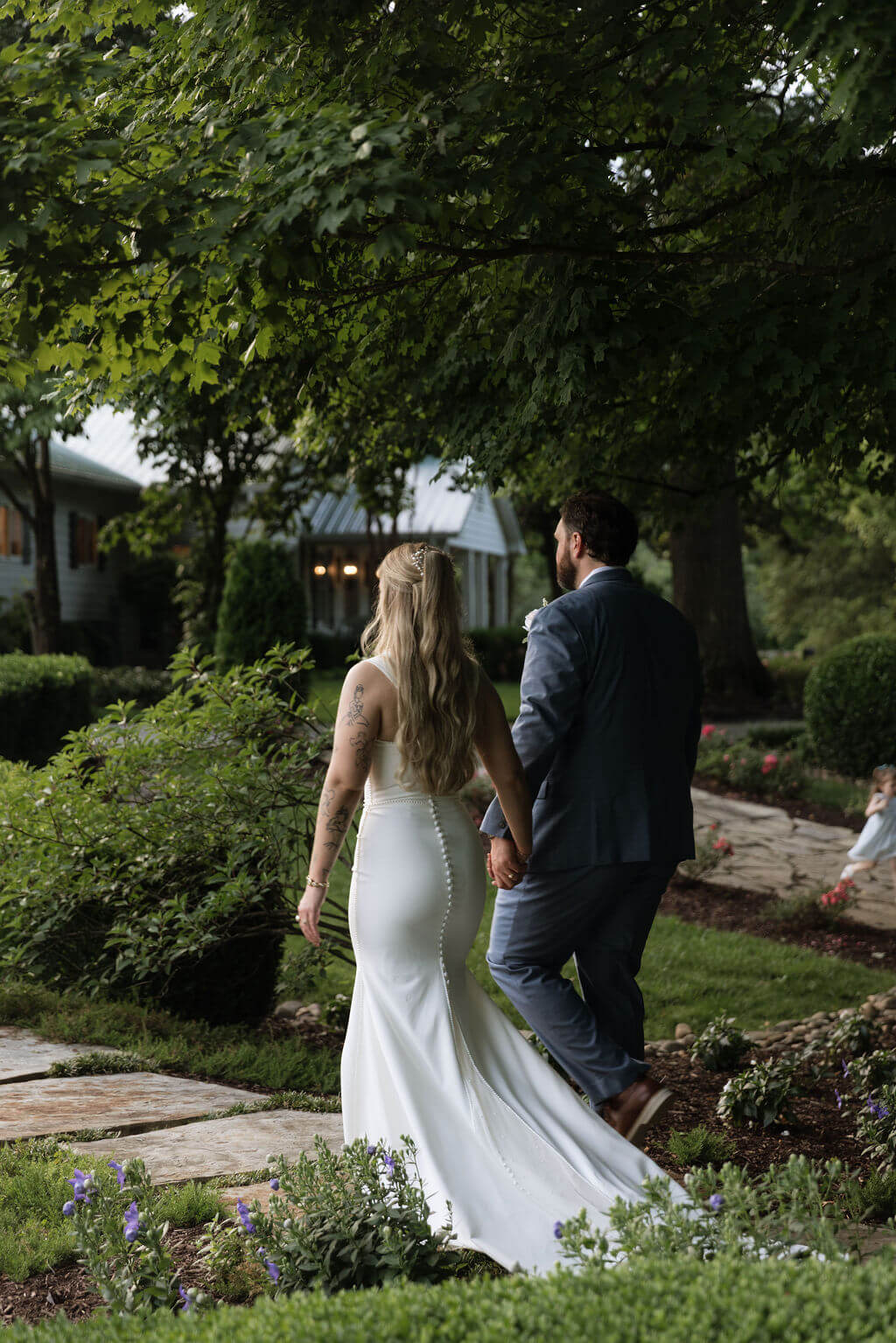 Newlyweds walking hand in hand through a landscaped garden after their wedding ceremony.