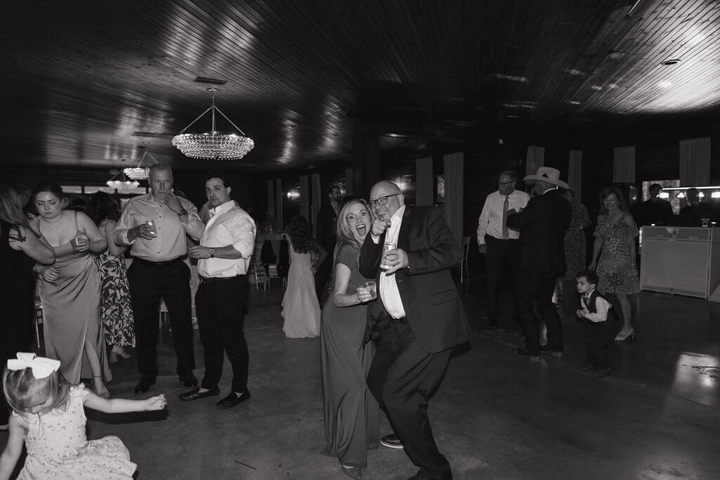 Black-and-white candid photo of wedding guests dancing during an indoor reception.