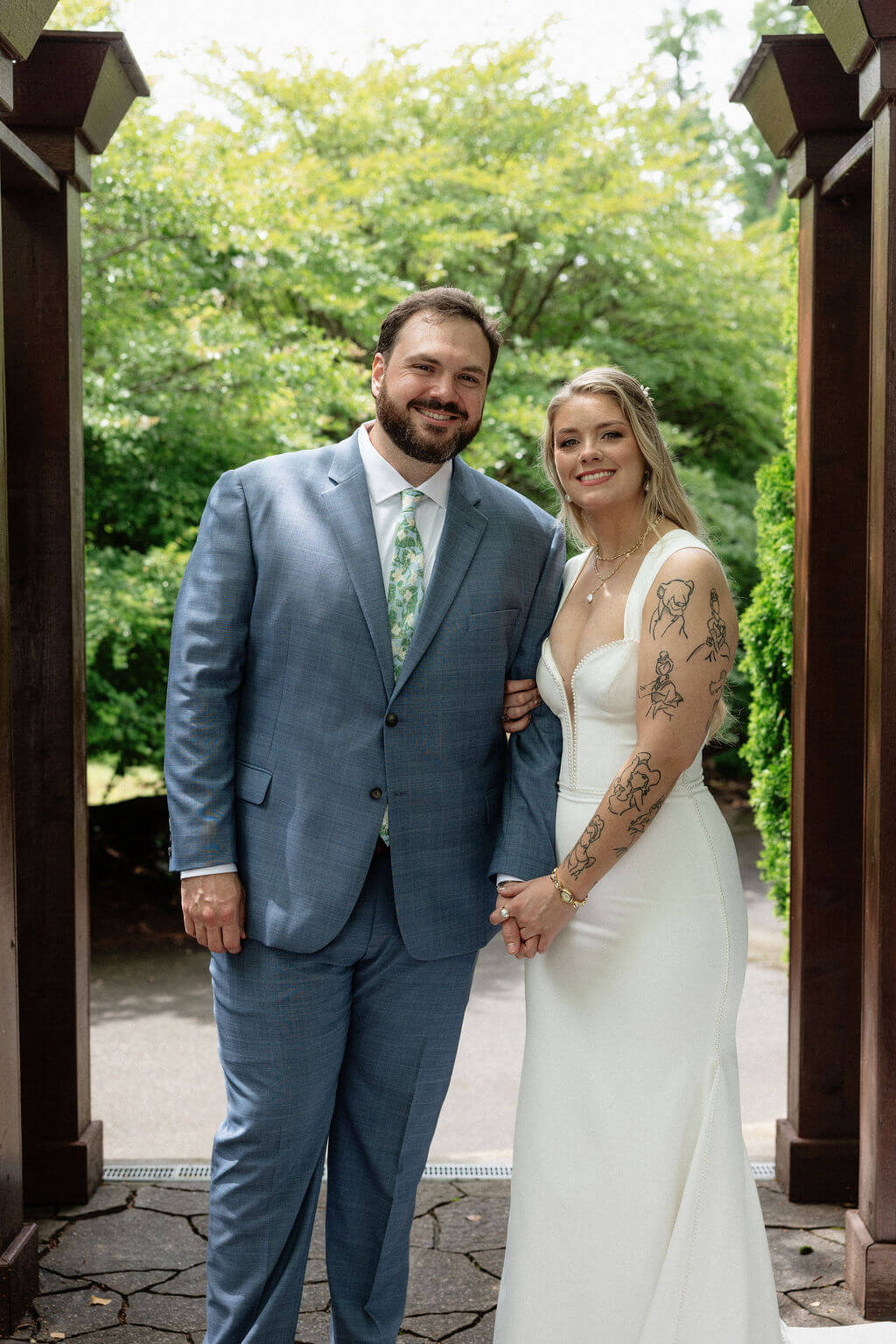 Newlyweds posing beneath a wooden garden arch surrounded by lush greenery.