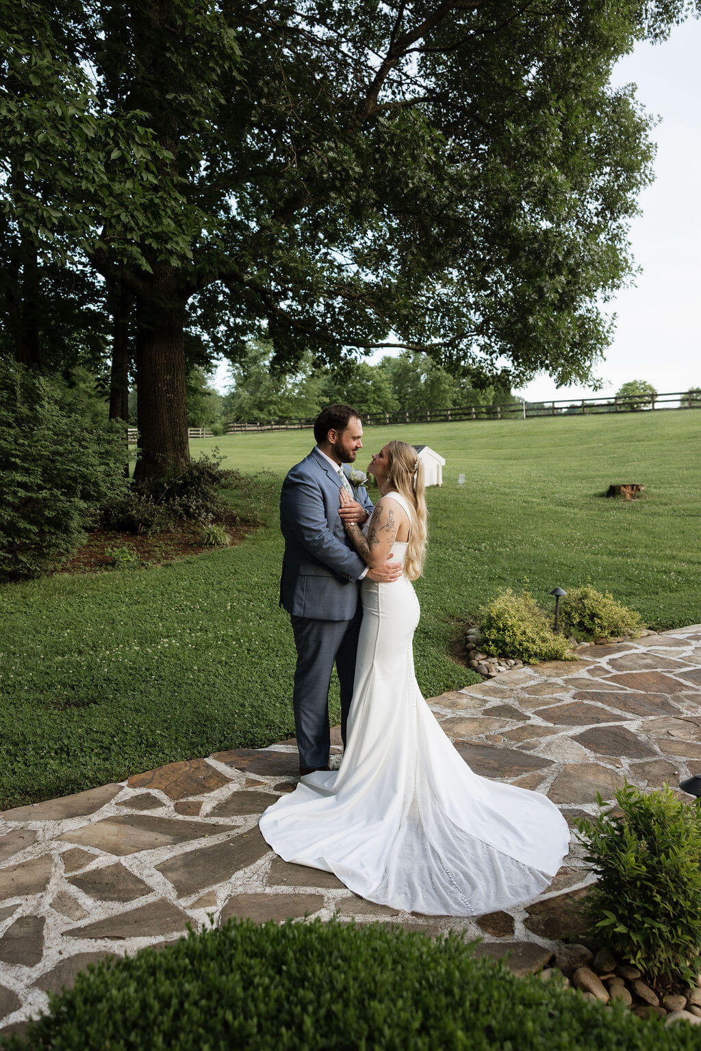 Groom embracing the bride on a stone garden path surrounded by manicured greenery.