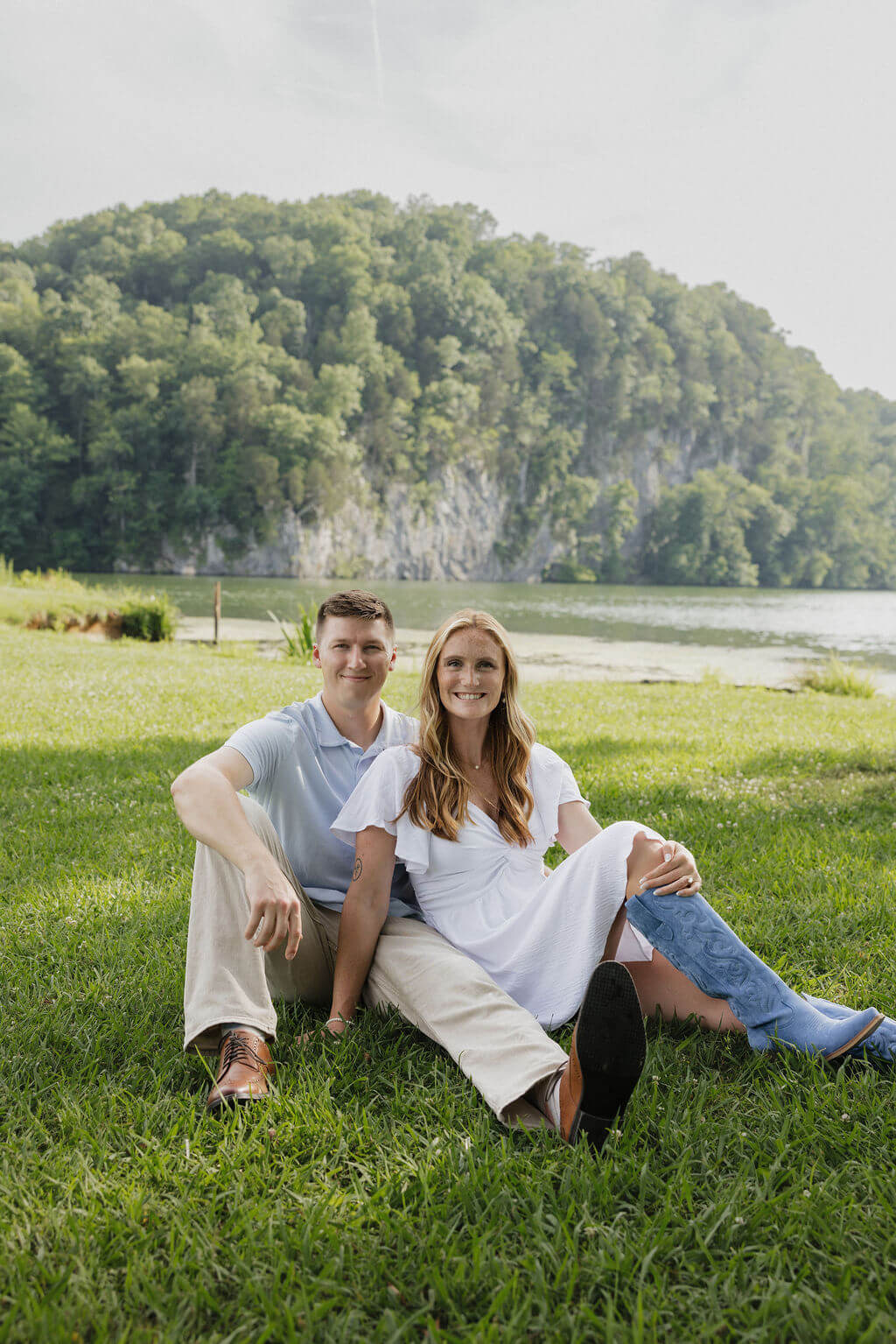 Engaged couple sitting together in the grass beside a lake during their Knoxville engagement session.