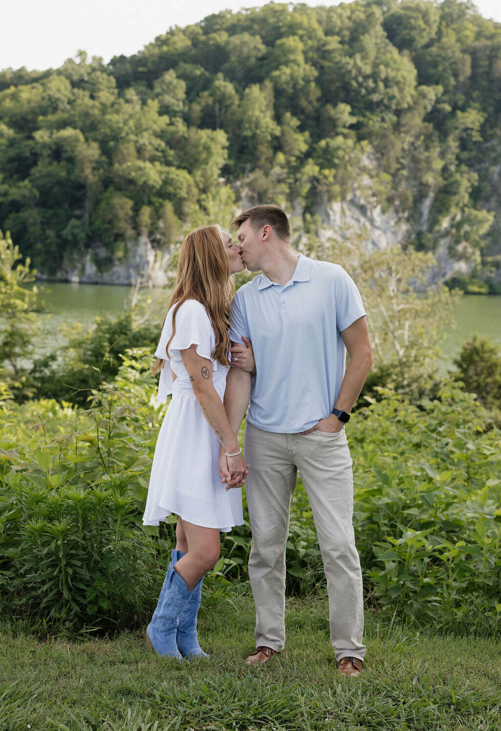 Couple standing together in front of a lake and wooded rocky hillside.