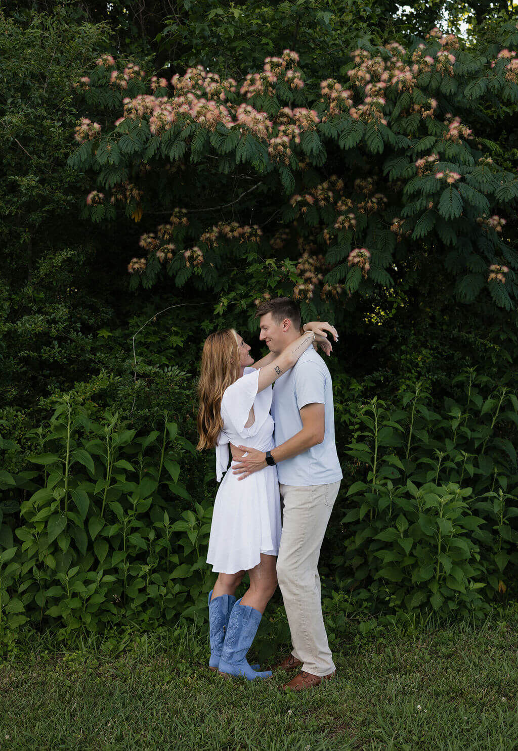 Couple kissing beneath flowering trees during a summer engagement session.